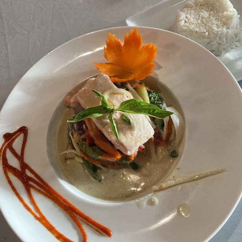 Thai green curry with fish, vegetables, basil, and a carrot garnish, served with rice.