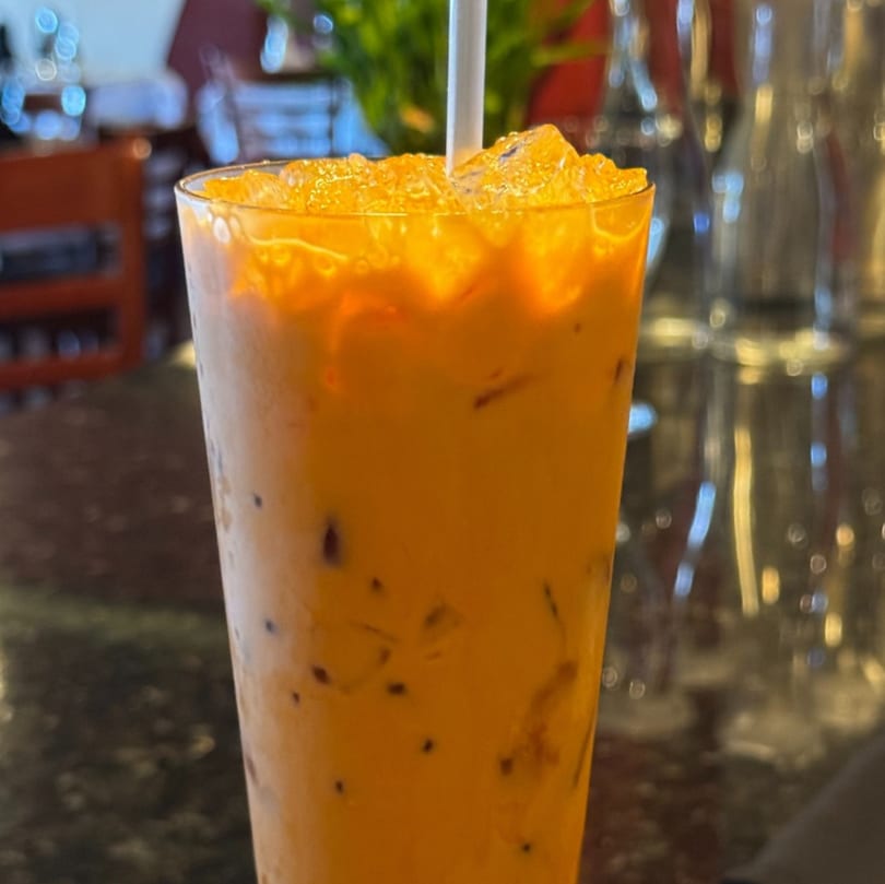 A tall glass of iced Thai tea with a white straw, filled with ice and a creamy orange drink.