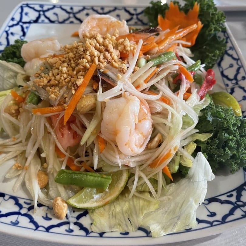 Jutamas Thai Restaurant's papaya salad with shrimp, peanuts, carrots, and lime on a decorative plate.