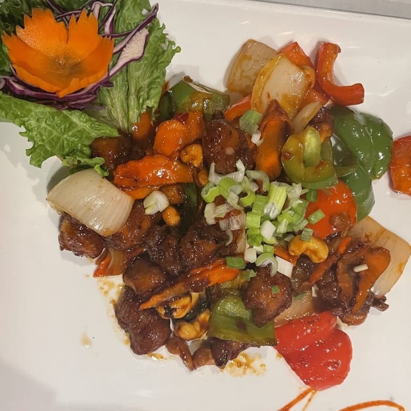 Cashew chicken stir-fry with bell peppers, onions, and scallions, garnished with a carved carrot.
